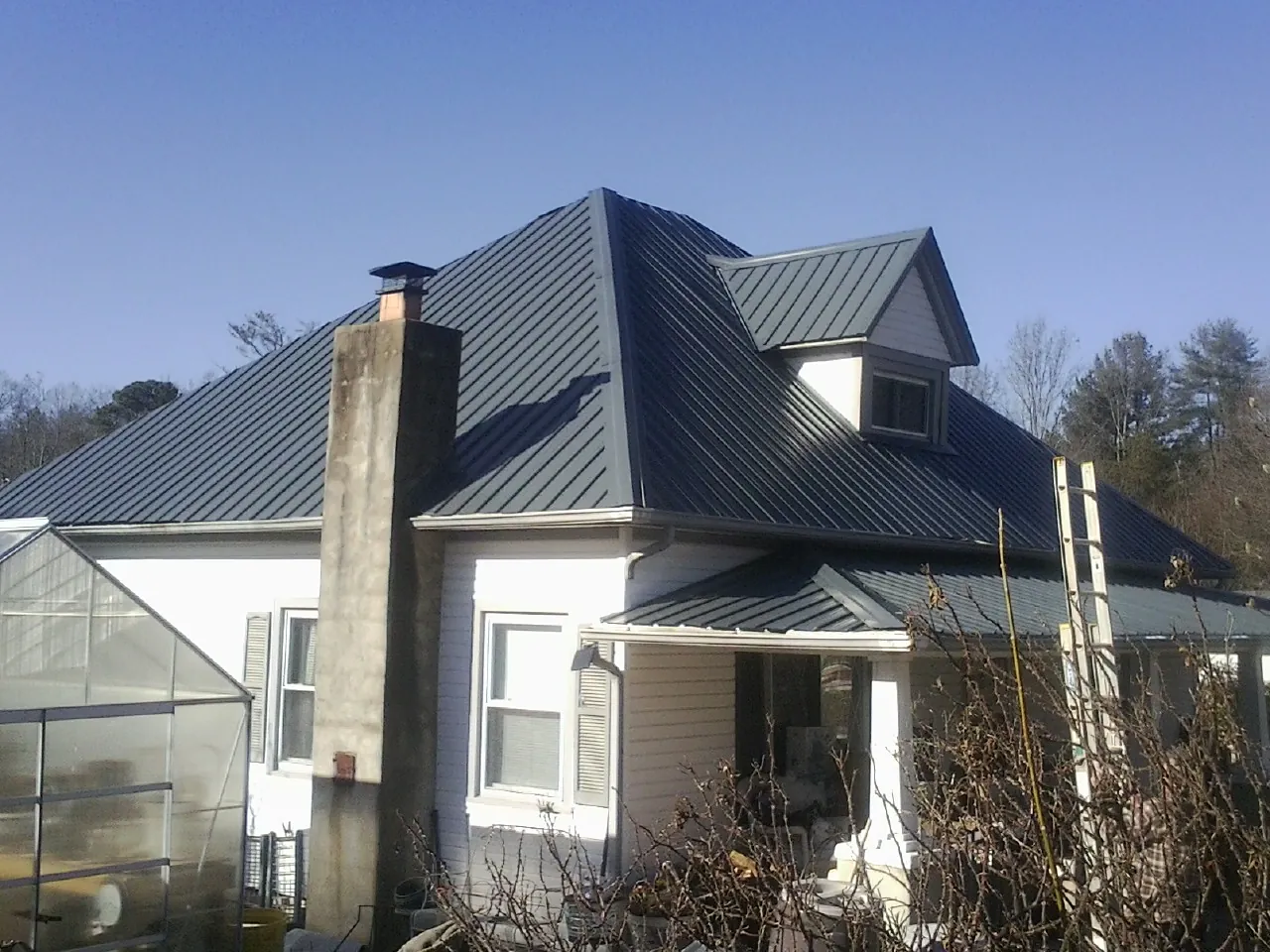 Dark blue standing seam metal roof on a white farmhouse with dormer — Slate & Tile Roof Repair by Roofing Brothers in Ucon