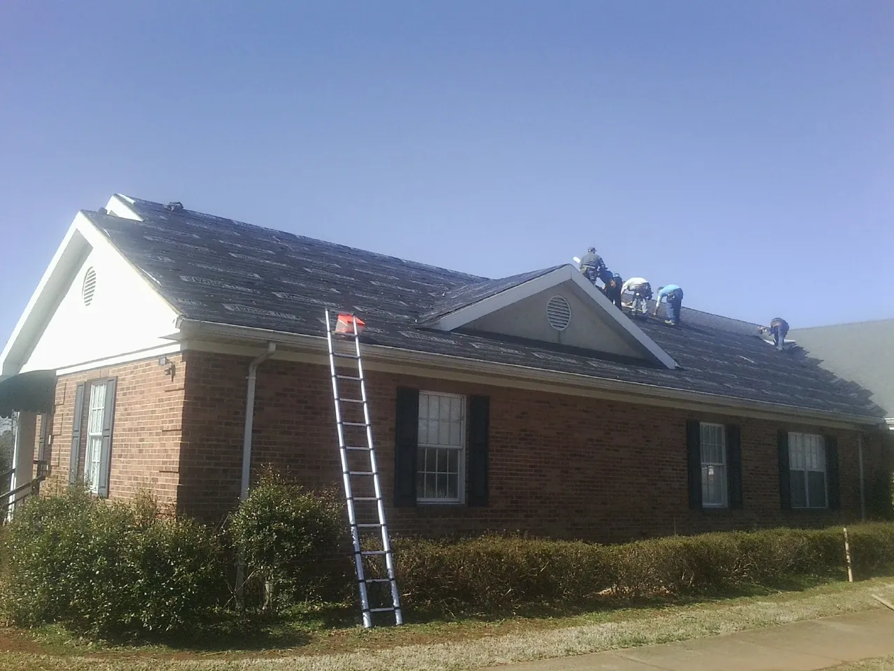 Crew tearing shingles off a brick ranch roof with a ladder set — Emergency Roof Repair work by our crew in Ucon