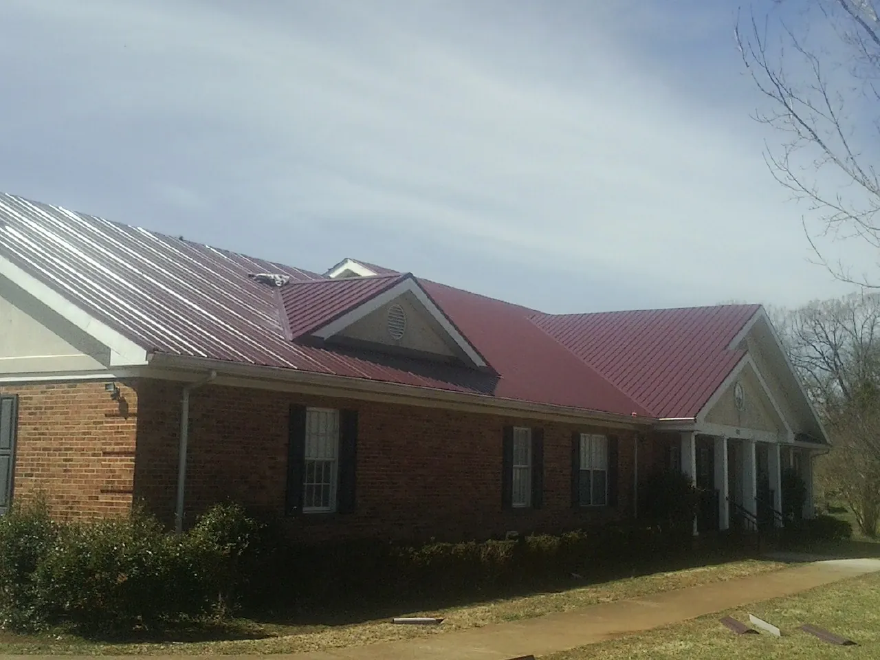 Red metal roof with gabled entries on a long brick building, from a Hail Damage Roof Repair job in Ucon