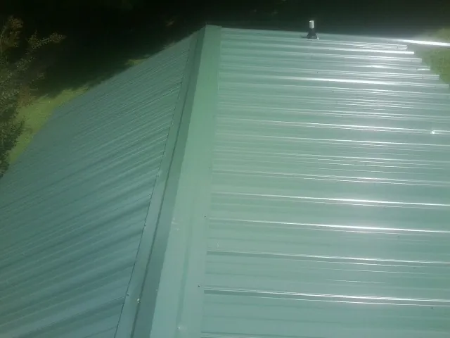 New green metal panels meeting at the ridge of a roof — Flat Roof Repair work by our crew in Ucon