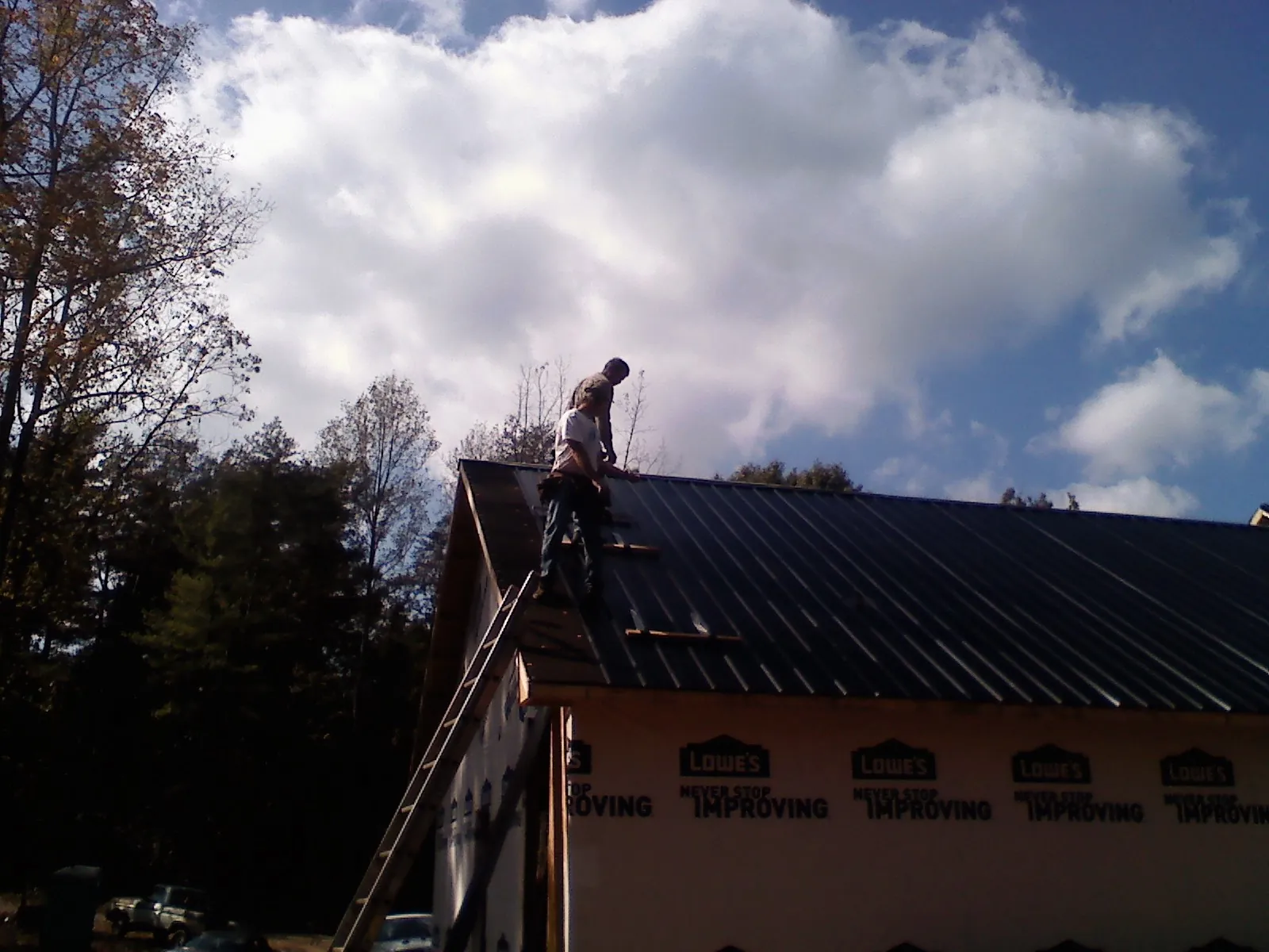 Roofer fastening dark metal panels high against a cloudy sky, from a Roof Inspection job in Ucon