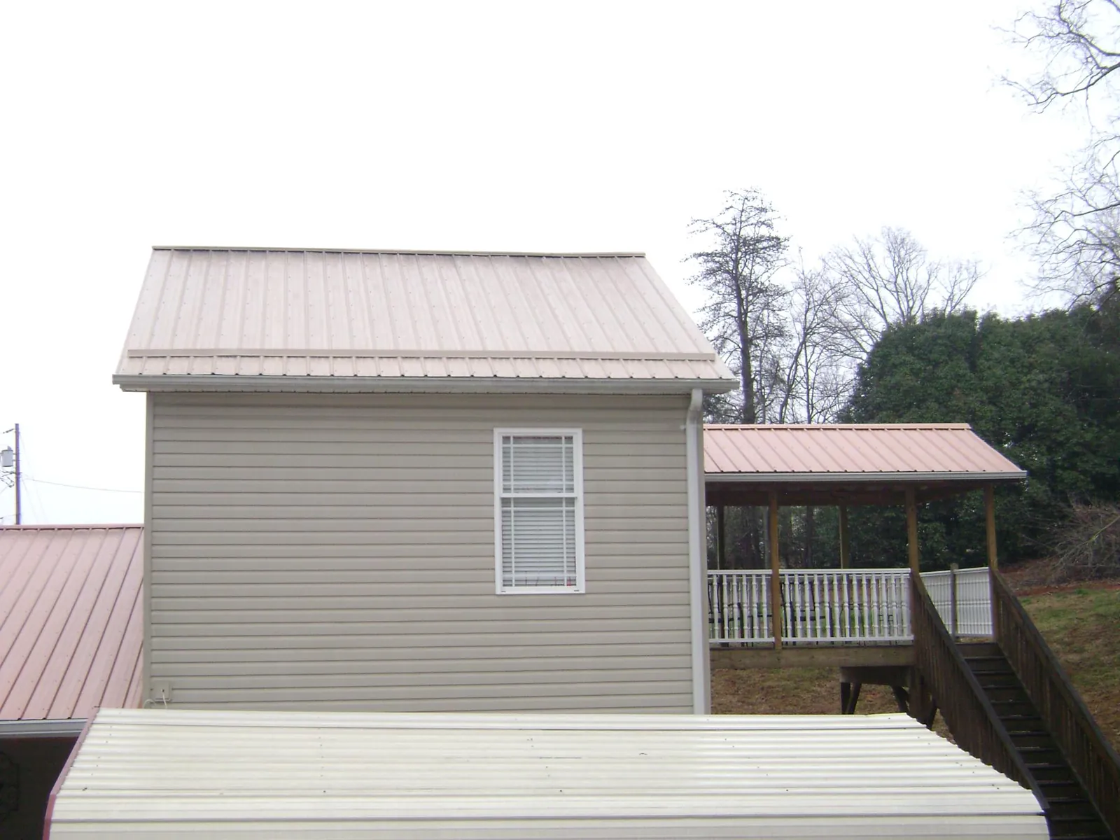 Tan metal roofs on a two story addition and attached porch, from a Roof Replacement job in Ucon